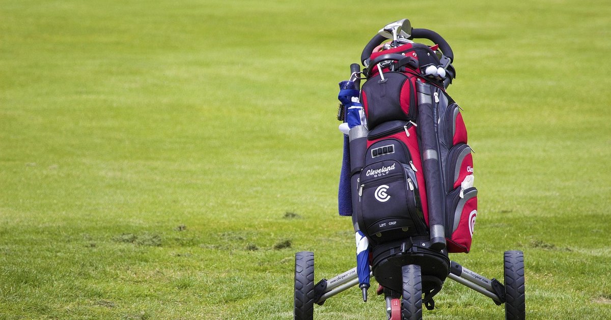 Golf bag full of clubs on a push cart on the fairway