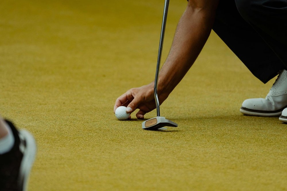 Golfer setting a ball down on the green next to a putter
