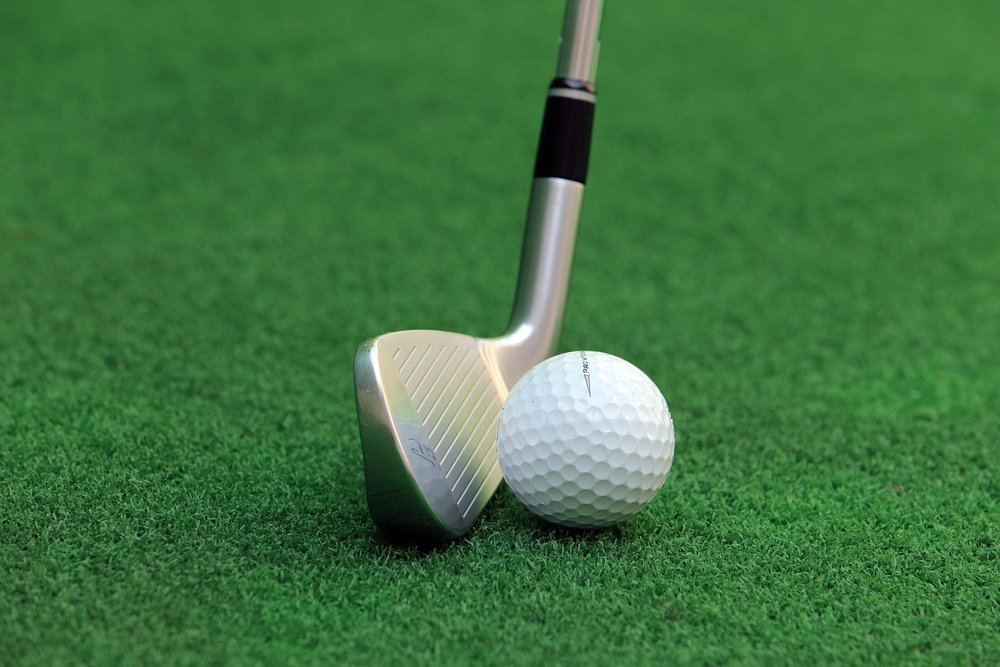 Close-up of a clean iron head behind a golf ball on short grass