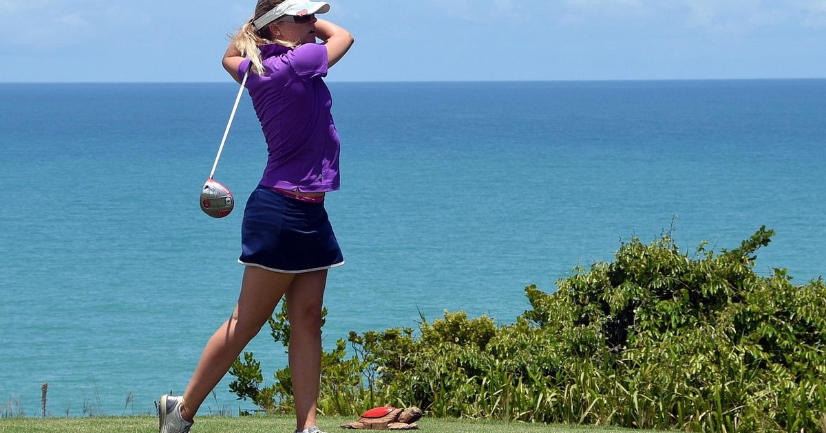 Golfer holding her finish after a tee shot on a course above the sea