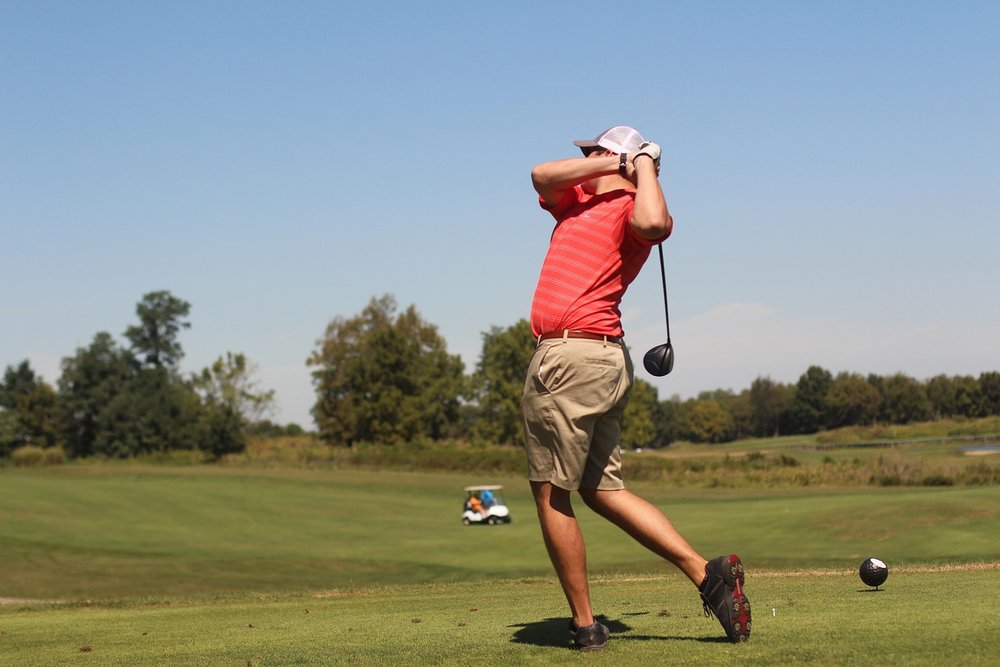 Golfer in a red shirt watching the flight of his tee shot