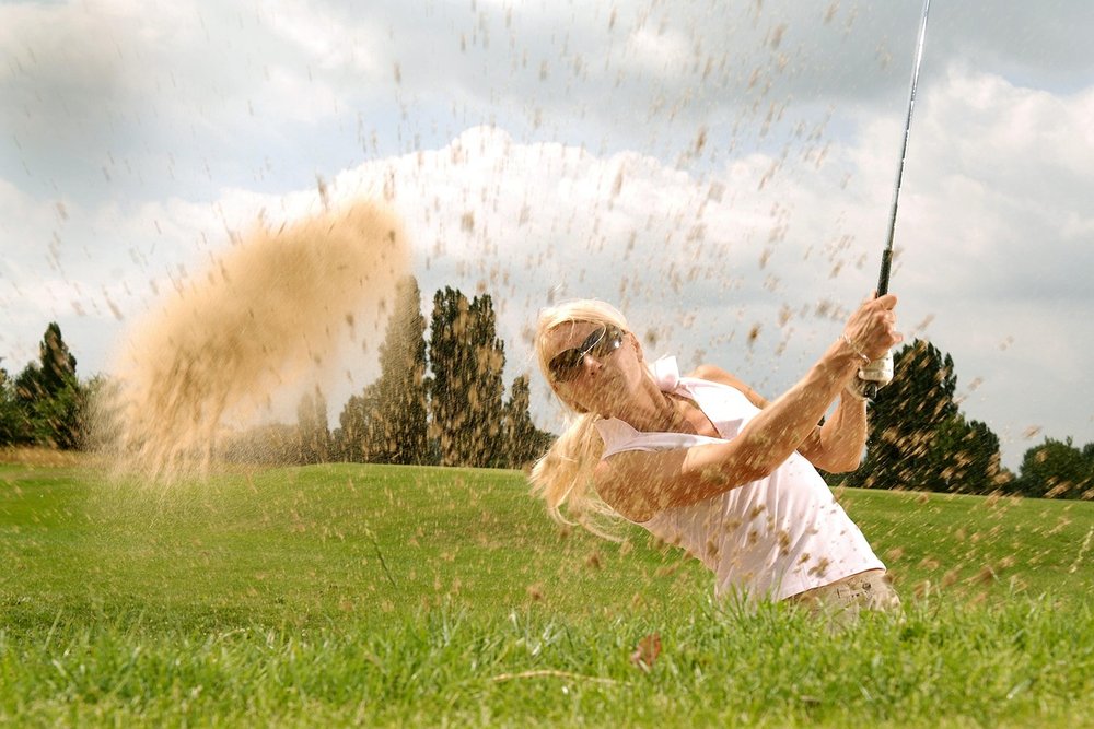 Woman splashing a ball out of a greenside bunker in a spray of sand