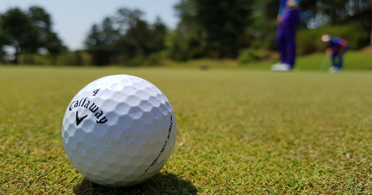 Golf ball on the fairway with golfers walking in the background