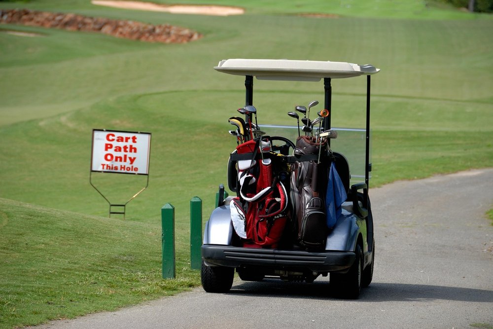 Golf cart with a bag parked on a cart path beside a sign