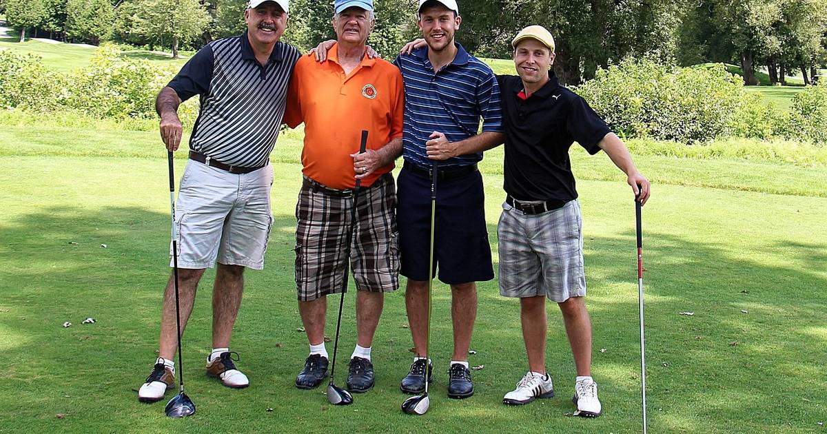Four golfers posing together with their clubs on a course
