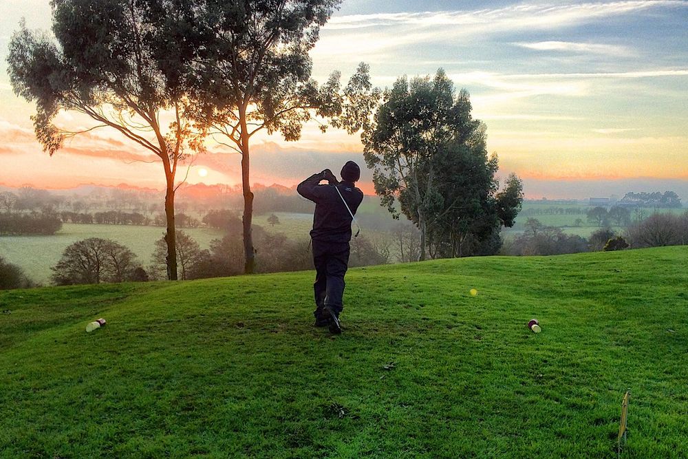 Golfer swinging on a hillside course at sunset