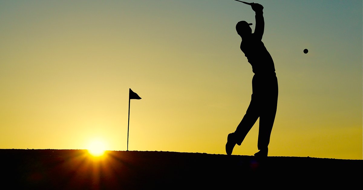 Silhouette of a golfer finishing a swing at sunset near a flag