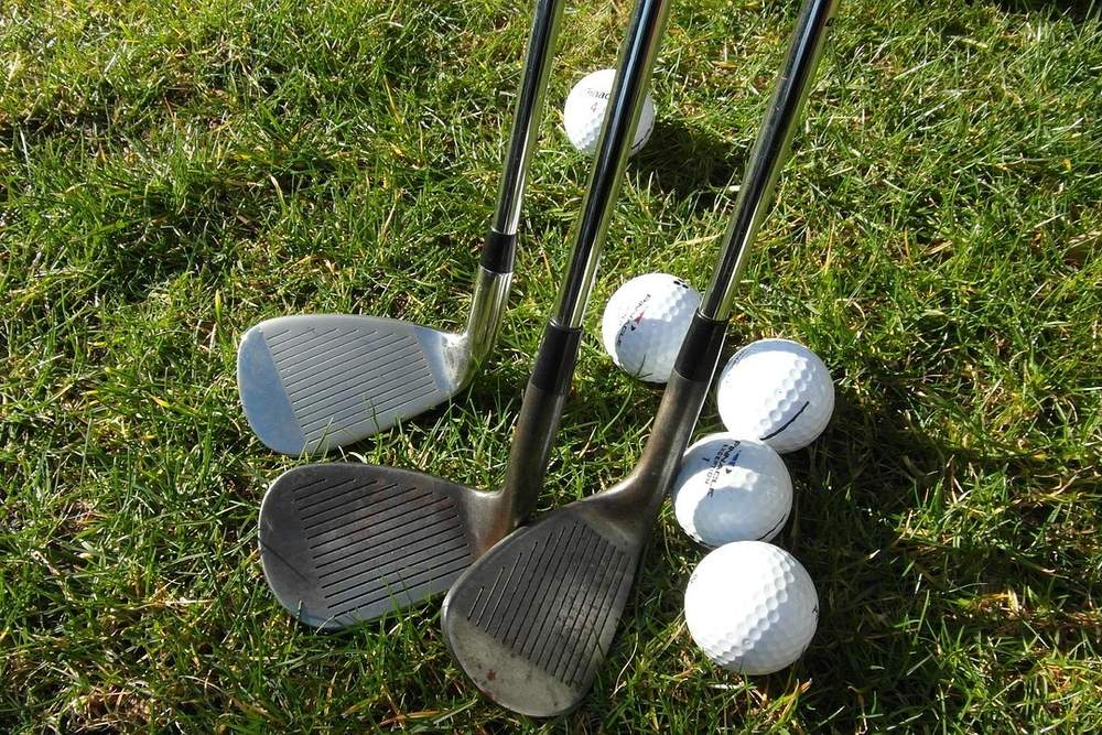 Three wedges lying on the grass beside a few golf balls